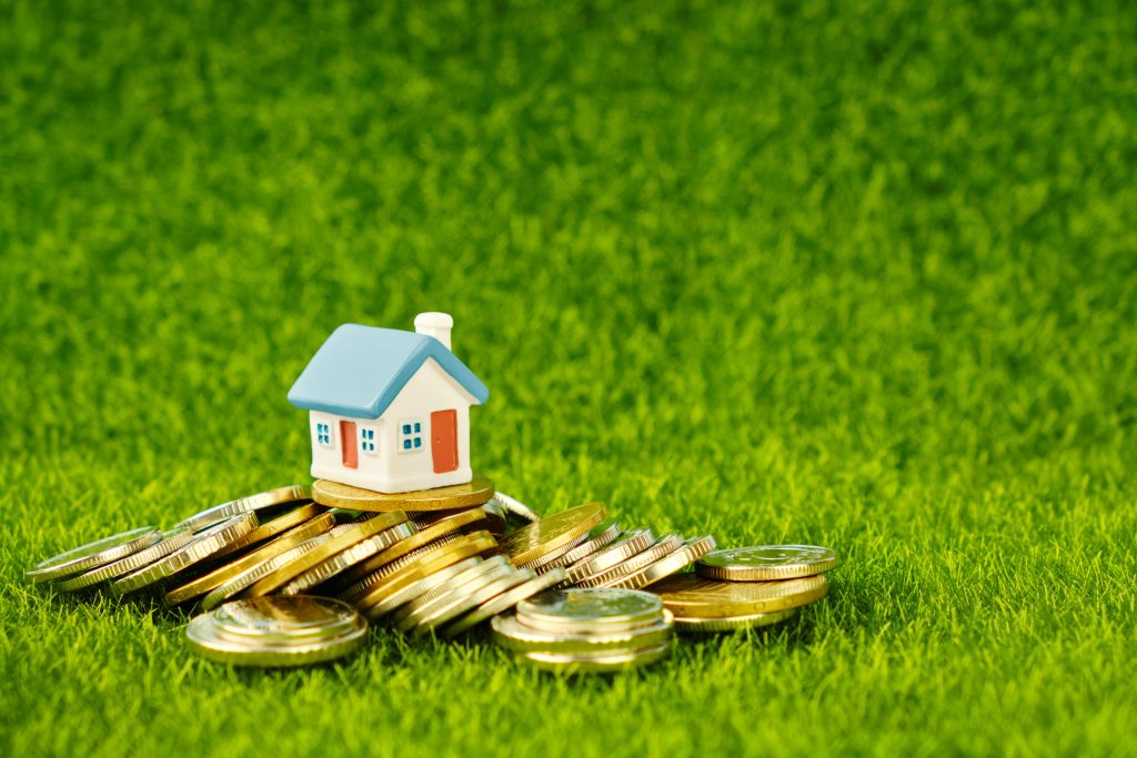 Inversiones inmobiliarias, imagen de una casa encima de una pila de monedas en referencia a la inversión de propiedades.